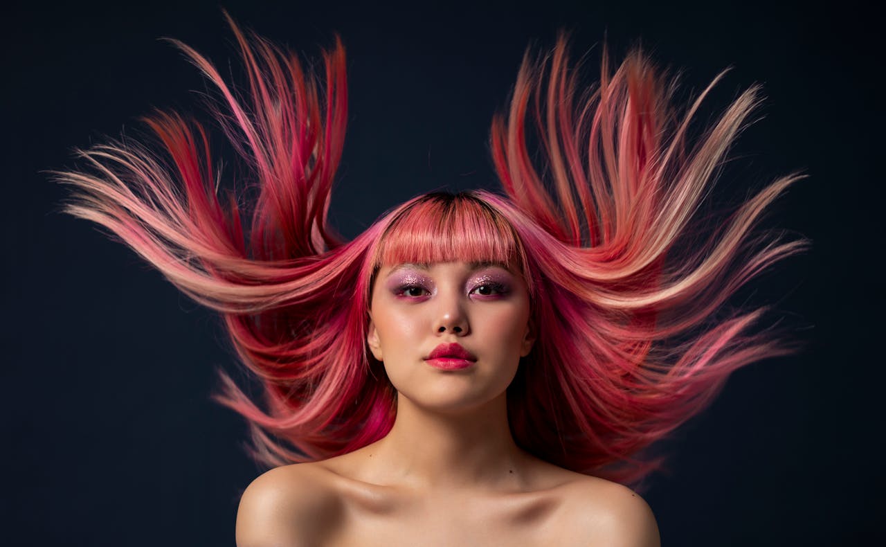 Dynamic portrait of a pink-haired model with hair in motion against a dark background.