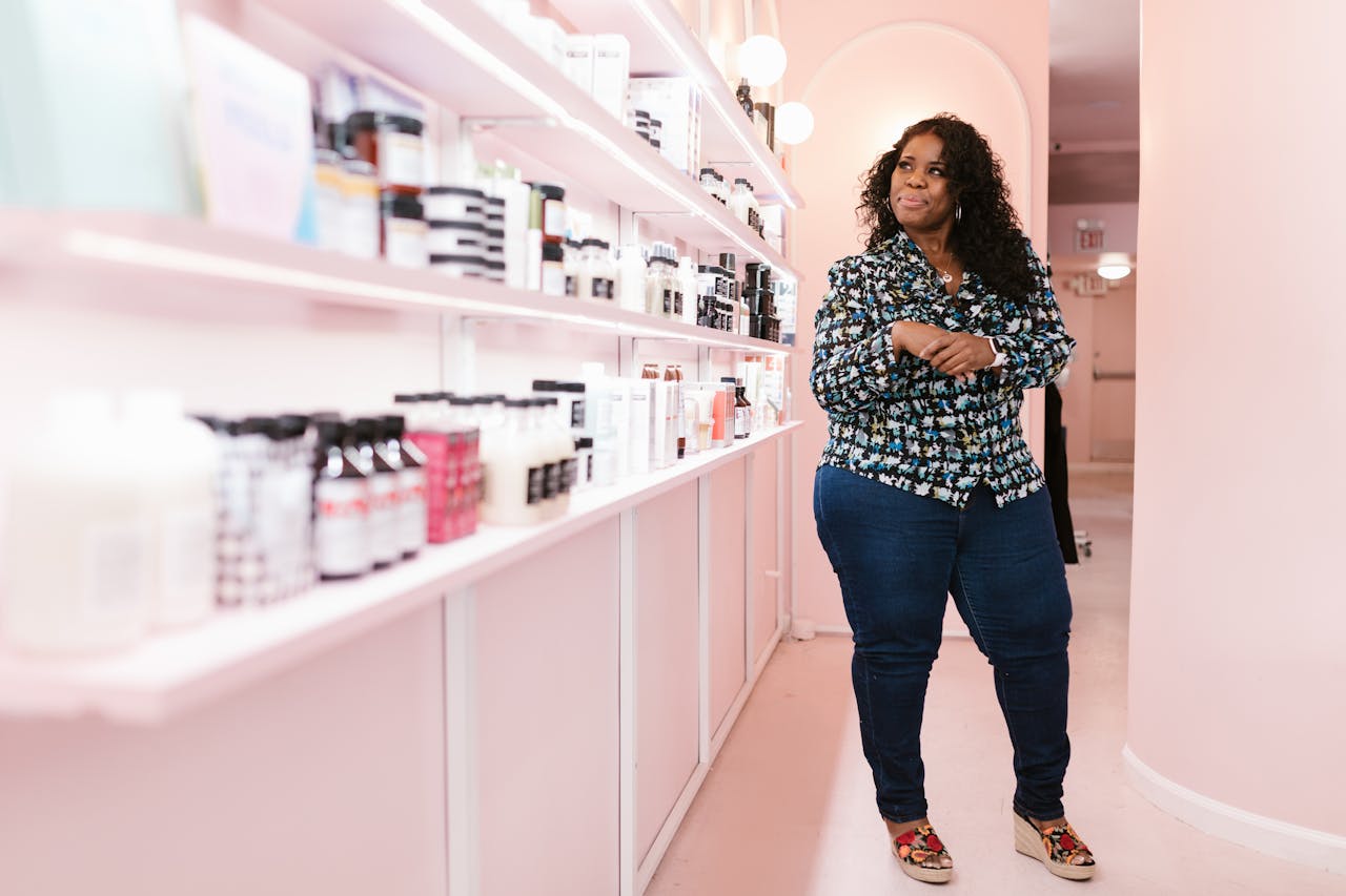 Woman standing in a modern beauty shop, smiling confidently beside shelves of cosmetics.